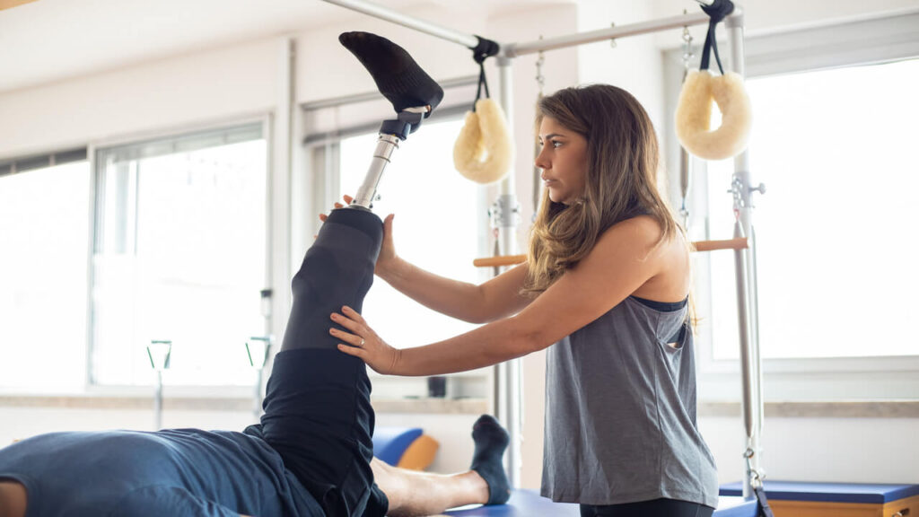 A woman assisting a man with a prosthetic leg during physical therapy indoors