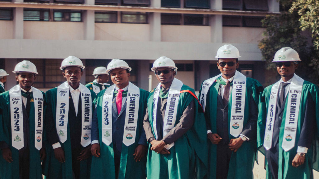 Group of chemical engineering graduates in hard hats and gowns celebrating their achievement