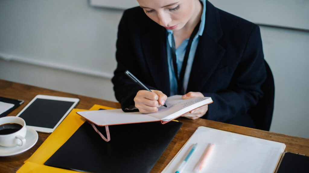 Professional businesswoman concentrating on writing notes at a work desk indoors