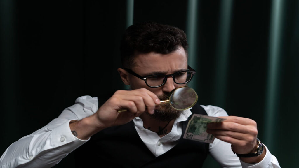 What Is Forensic Psychology-Focused adult inspecting a banknote closely with a magnifying glass indoors