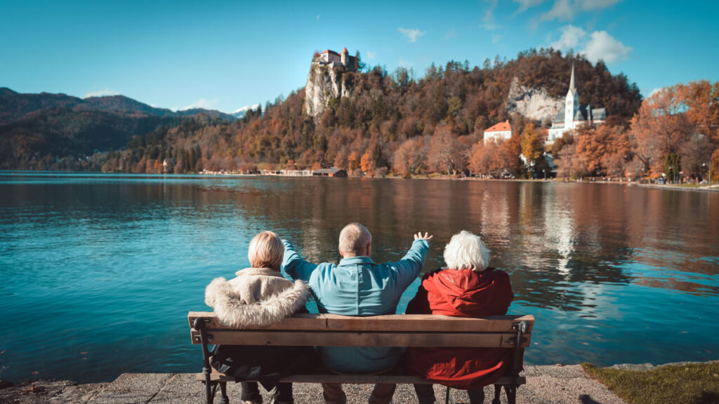 Senior people sitting on a bench by Lake Bled, enjoying the scenic lake and autumn colors in Slovenia